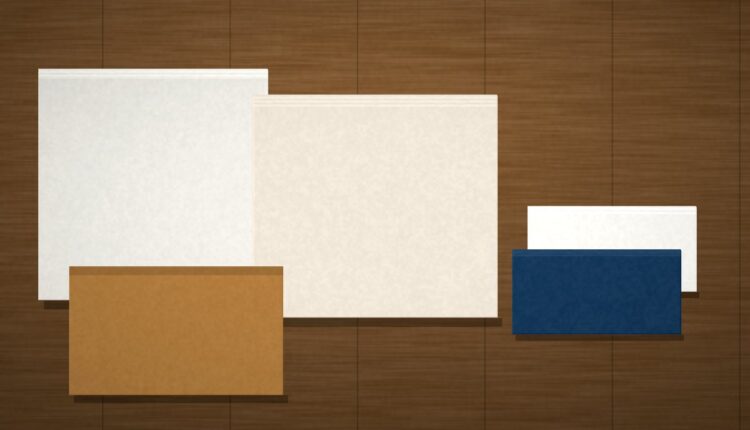 Stacked blank flyers, catalogs, and a kraft delivery carton on a commercial work table in daylight, no people or text